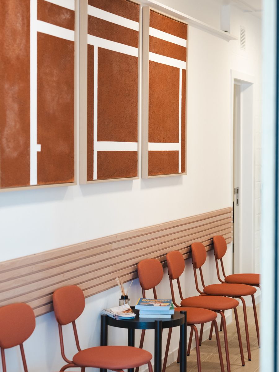 La salle d'attente, chaises terracotta alignées le long d'un lambris de bois clair